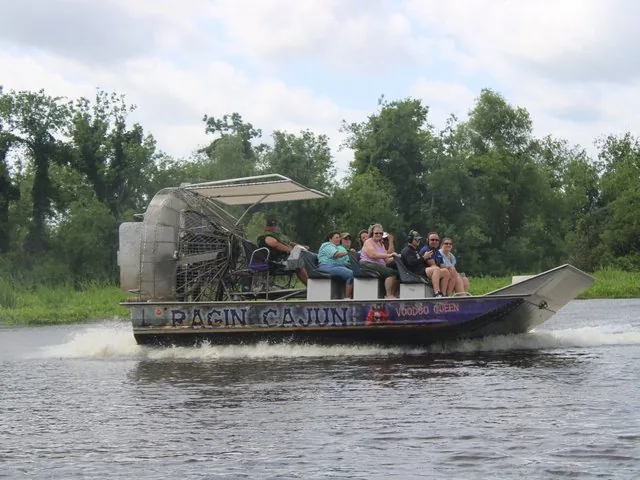 An airboat carrying several passengers speeds across the water in the swamp.