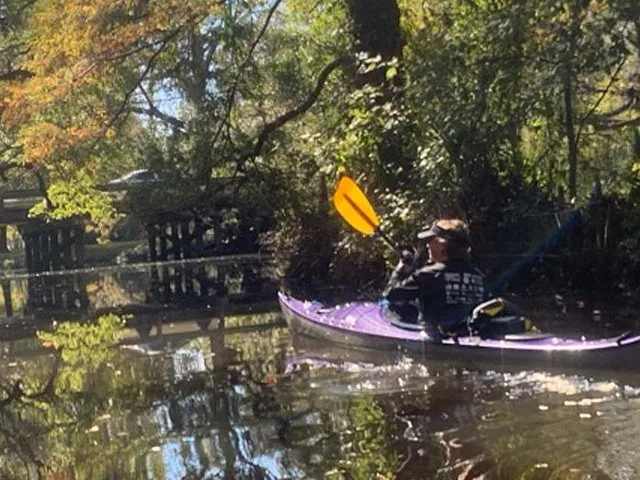 A person kayaking on a calm river with a bridge in the background.