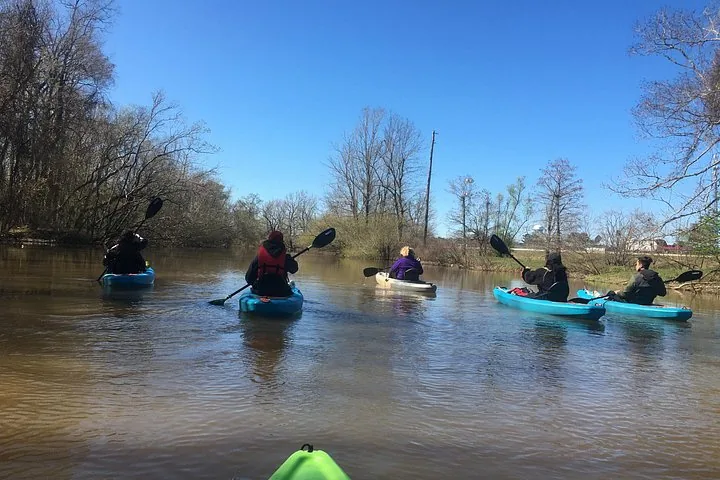 A group of people kayaking down a wide river under a clear sky.